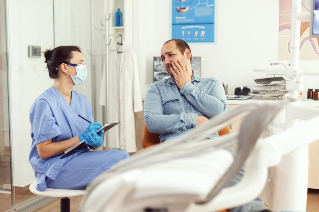 asistente dental explicando si se puede hacer un conducto radicular en una visita mientras un paciente con dolor de muelas escucha