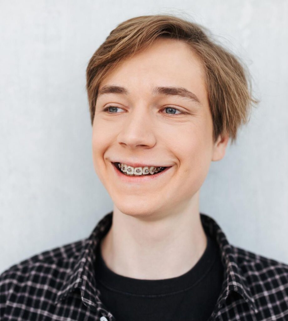 Retrato de un joven sonriente con frenos metálicos de pie y felizmente mirando a un lado sobre fondo blanco.