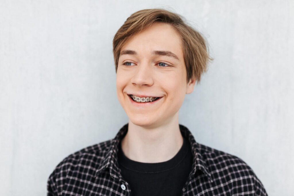 retrato joven sonriente. con frenillos de pie felizmente mirando a un lado fondo blanco feliz de saber si necesito frenillos si tengo una sobremordida