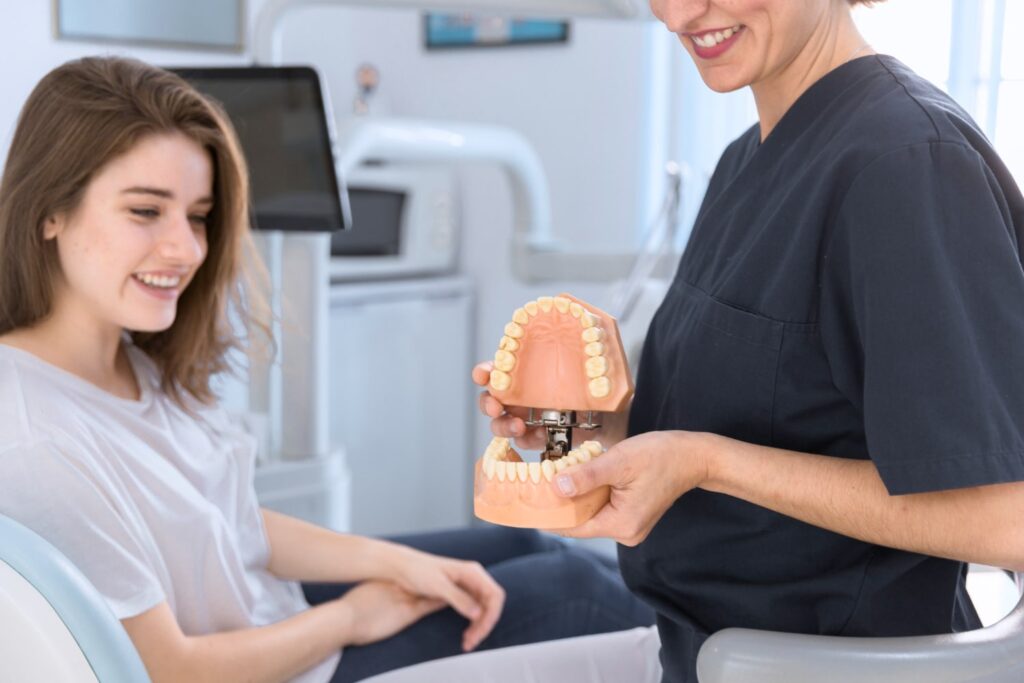 Dentista en primer plano mostrando a un paciente un modelo dental para explicar el costo de las coronas dentales