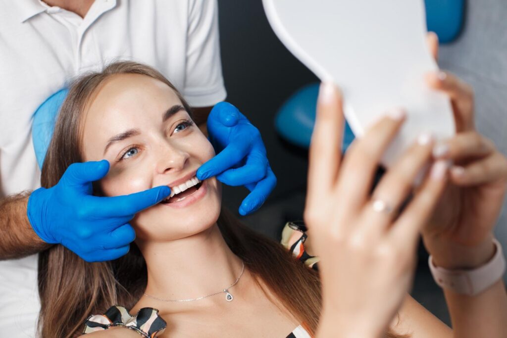 Young female dental patient observing the results of her professional teeth whitening in South Carolina while holding a mirror with both hands