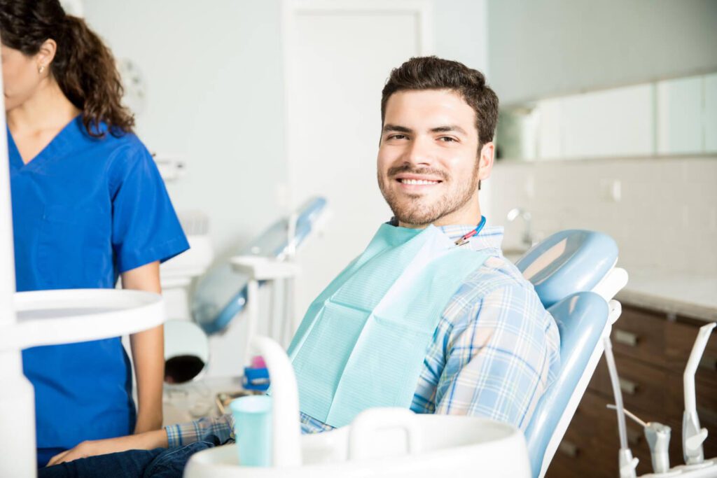 portrait smiling man sitting chair while female dentist working clinic