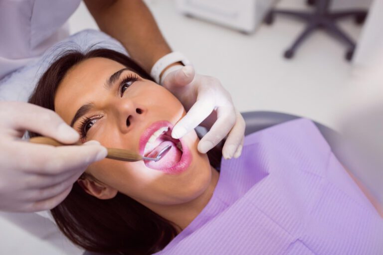 Dentist examining female patient teeth with a mouth mirror explaining how long does teeth sensitivity last