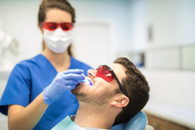 Dentist checking mid adult man with ultraviolet light in dental clinic explaining how to whiten teeth without enamel damage