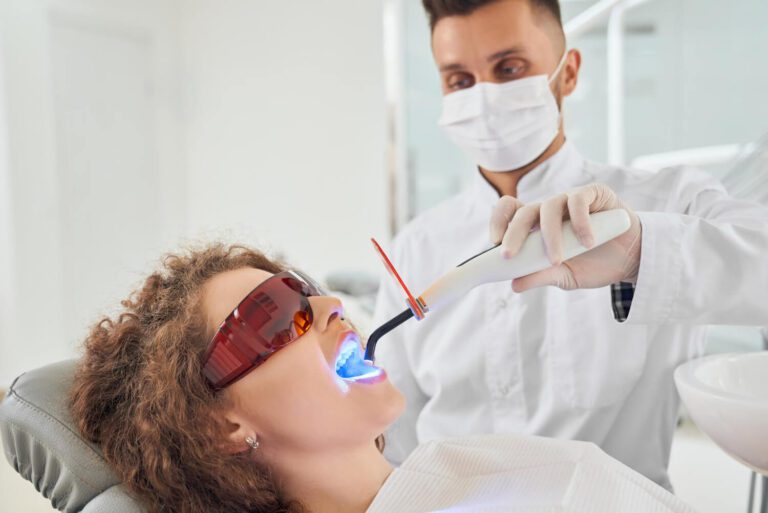 Girl lying on chair while dentist keeping ultraviolet tool feeling teeth whitening and tooth sensitivity