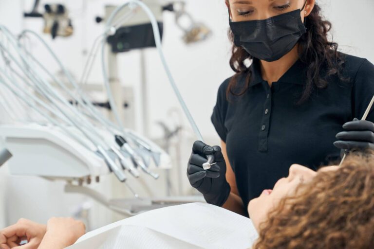 Skilled dentist in uniform and mask curing teeth of patient explaining how long does it take to heal from root canal